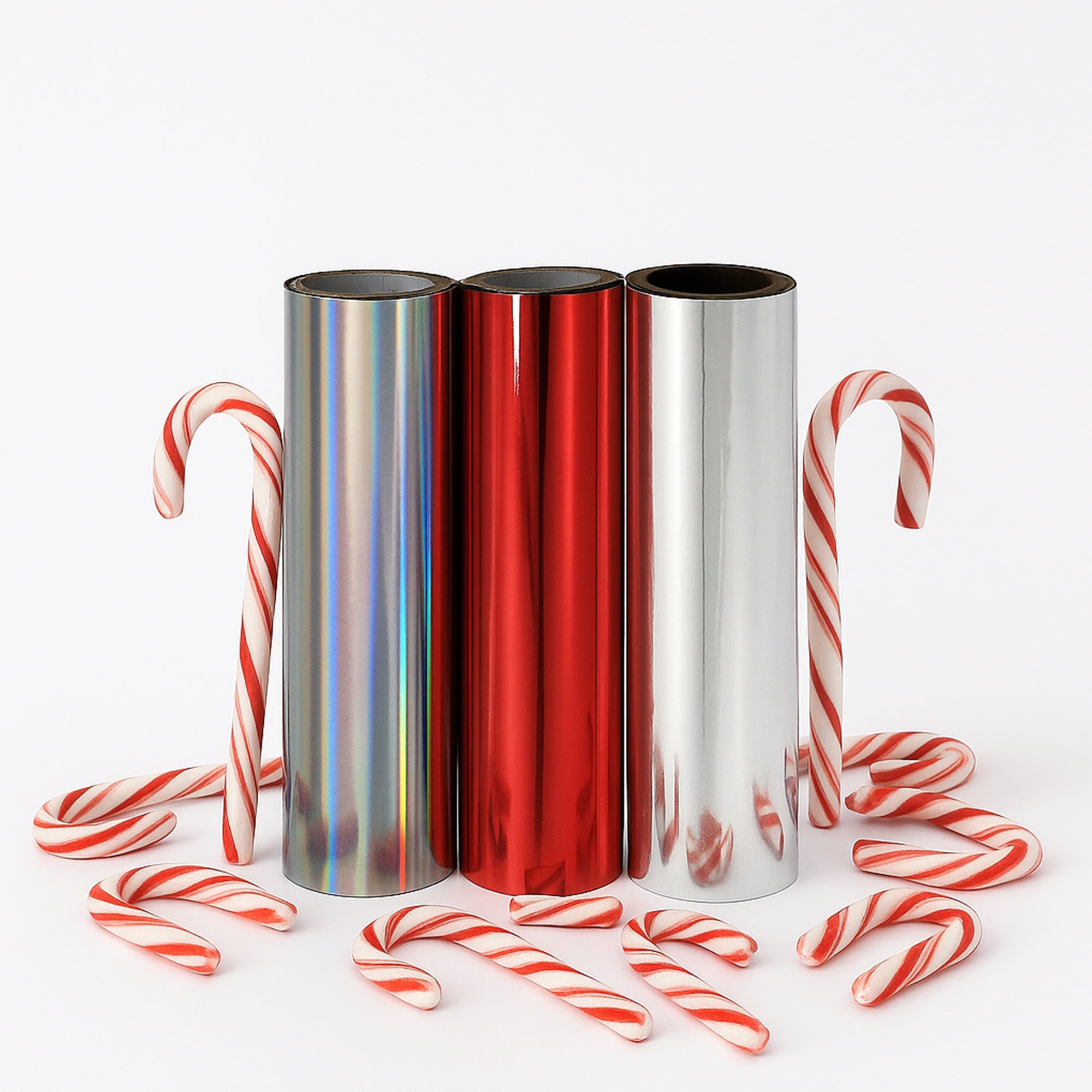 Three toner-foil rolls—holographic silver, metallic red and metallic silver—surrounded by red-and-white candy canes on a white background.